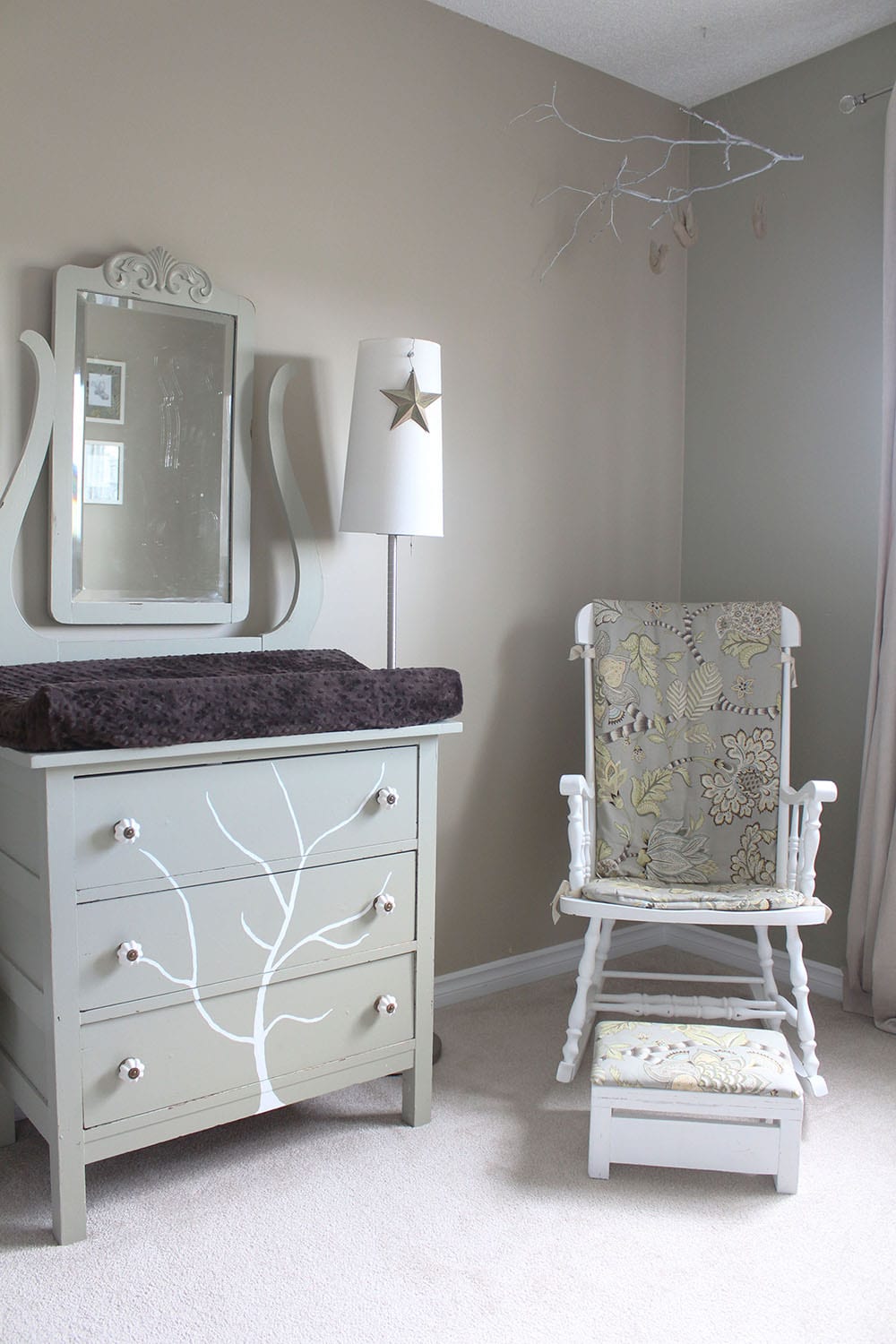 A neutral baby bedroom featuring a handpainted tree dresser and refinished rocking chair.