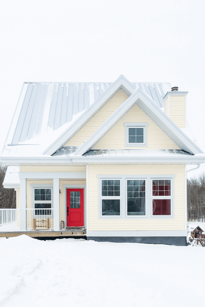 Yellow house with a red door in winter.