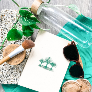 Various eco-friendly items - such as a glass water bottle and wooden sunglasses on a green fabric background.