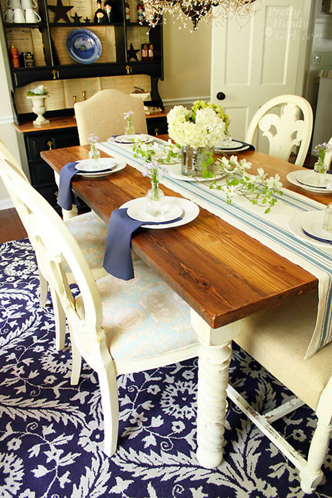 A wood dining table with white legs, set with white dishes and blue and white linens.