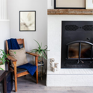 A wooden chair next to a vintage brass table and a minimalist white and black fireplace. 
