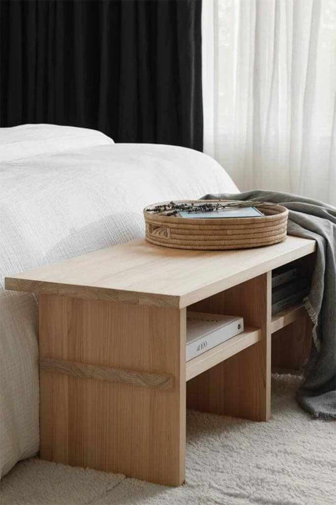 A wooden bench at the foot of a white bed.