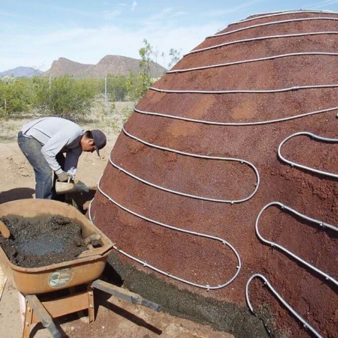 A man working on a small dome-shaped home made out of ferrock.