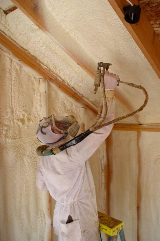 A person in protective gear spraying soy insulation into a ceiling cavity.