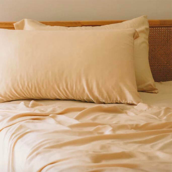 Light peach bedding on a bed with a woven headboard.