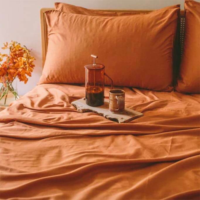 Terracotta bedsheets next to a table with orange flowers.