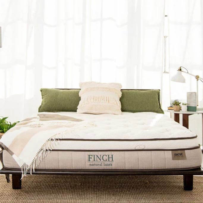 A white mattress with green text on it in a bright bedroom.