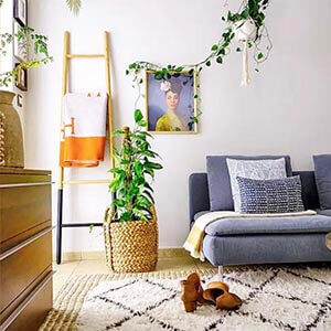 An eclectic living room with a blue couch, blanket ladder and vintage portrait on the wall.