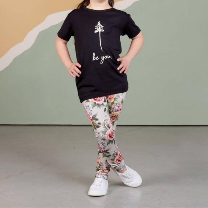 A child wearing floral leggings and a black tee with text be you.