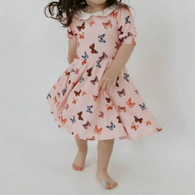 A child wearing a pink dress with butterflies on it.