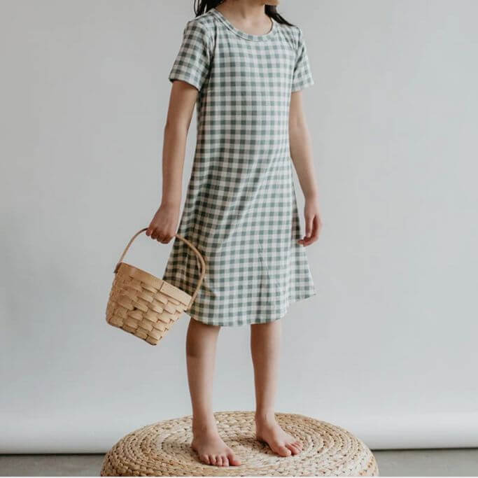 A child wearing a gingham pajama dress holding a basket.