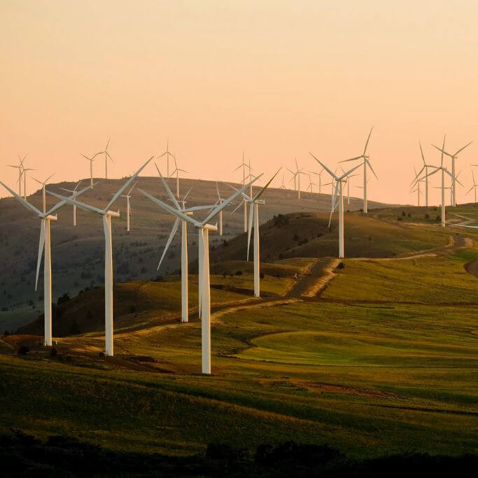 Many wind turbines on a hill at dusk.