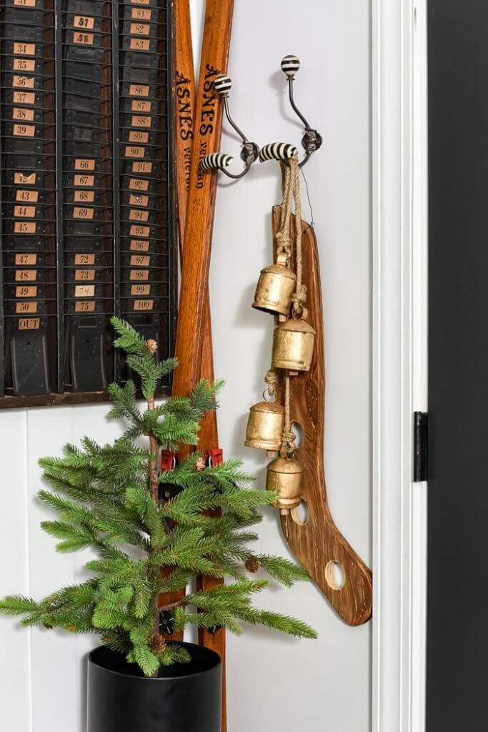 A vintage wooden stocking stretcher hanging on a wall with bells next to a small evergreen tree in a pot.