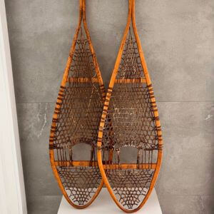A pair of wooden snowshoes propped against a grey wall.