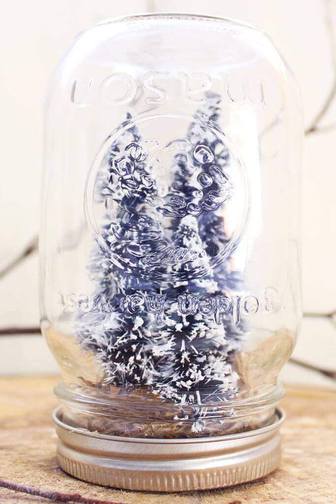 A handmade mason jar snow globe sitting on a tree slice.