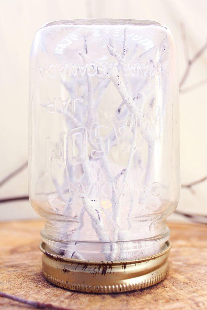 Handmade mason jar snow globe with white twigs inside.