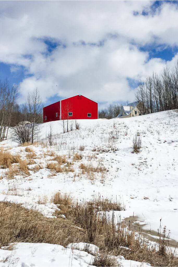 A red steel building next to a yellow house on top of a snow covered hill.