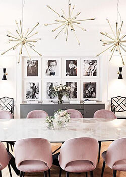A glam-inspired dining room with pink velvet chairs, black and white photos and three gold starburst pendant lights.