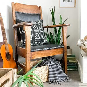 A vintage chair with a black and white pillow on it, surrounded by plants books and an old guitar.