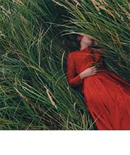 A photograph of a woman in a red dress in the grass.