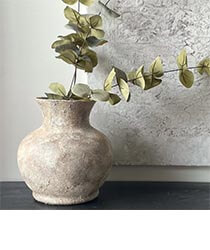 An off-white rustic vase with greenery in it.
