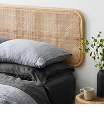 A woven headboard on a bed with dark grey and black bedding.