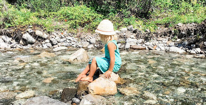 A little girl sitting on a rock in a creek.