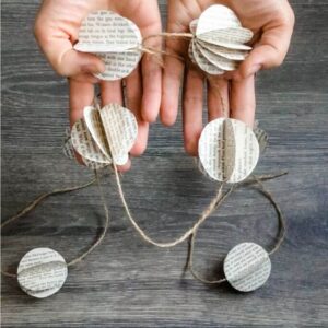 A closeup of a pair of hands holding a garland made of book page orbs and twine.