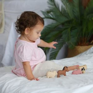 A baby sitting on a bed playing with toy farm animals.
