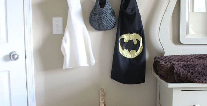 A kid's bedroom with a white wooden bench, a white shelf and a handmade superhero cape hanging on a hook.