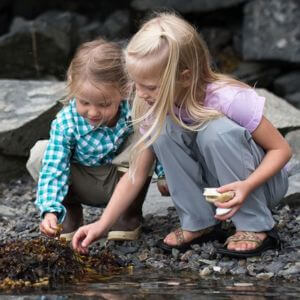 Two little girls playing in a stream wearing outdoor clothing.