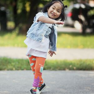 A little girl playing outside wearing colourful pants and a denim vest.