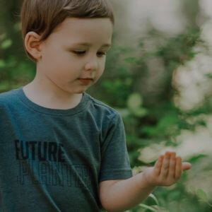 A little boy standing in a forest holding something in his hand.