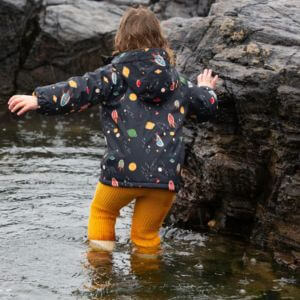 A young child in a raincoat playing in water.