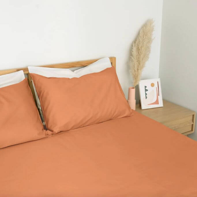 Orange-pink bedding on a simple wood bed frame.