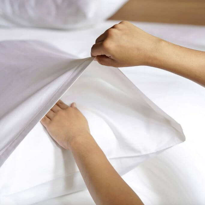 Closeup of a pair of hands putting a white pillowcase on a pillow.