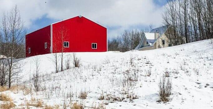 A red metal building atop a snow covered hill.