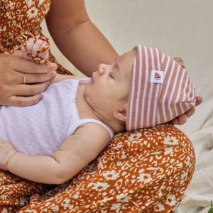 A baby in a striped hat laying on a woman's lap.