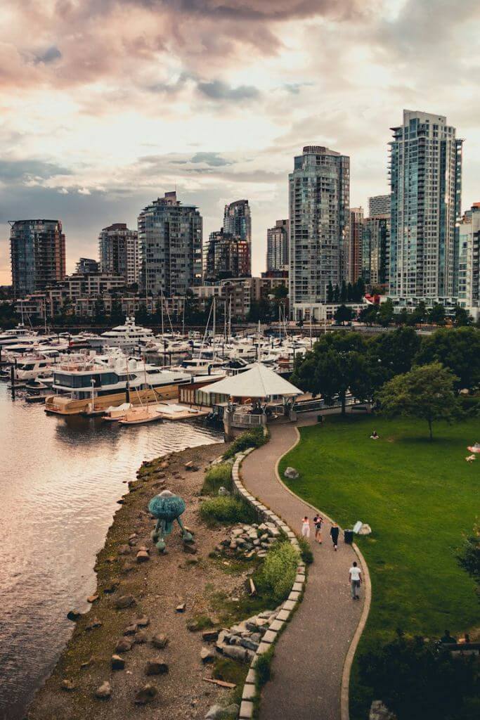 City of Vancouver skyline with people walking on a pathway next to water.