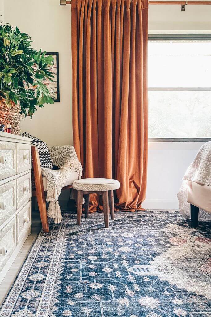 Bedroom with a large blue rug and orange curtains.