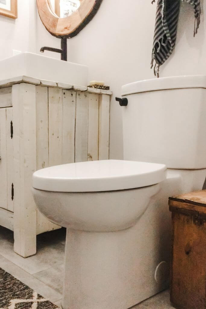 A toilet in a clean, bright, white bathroom with painted wood vanity and black fixtures.