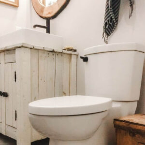A toilet in a clean, bright, white bathroom with a light wood vanity and black fixtures.