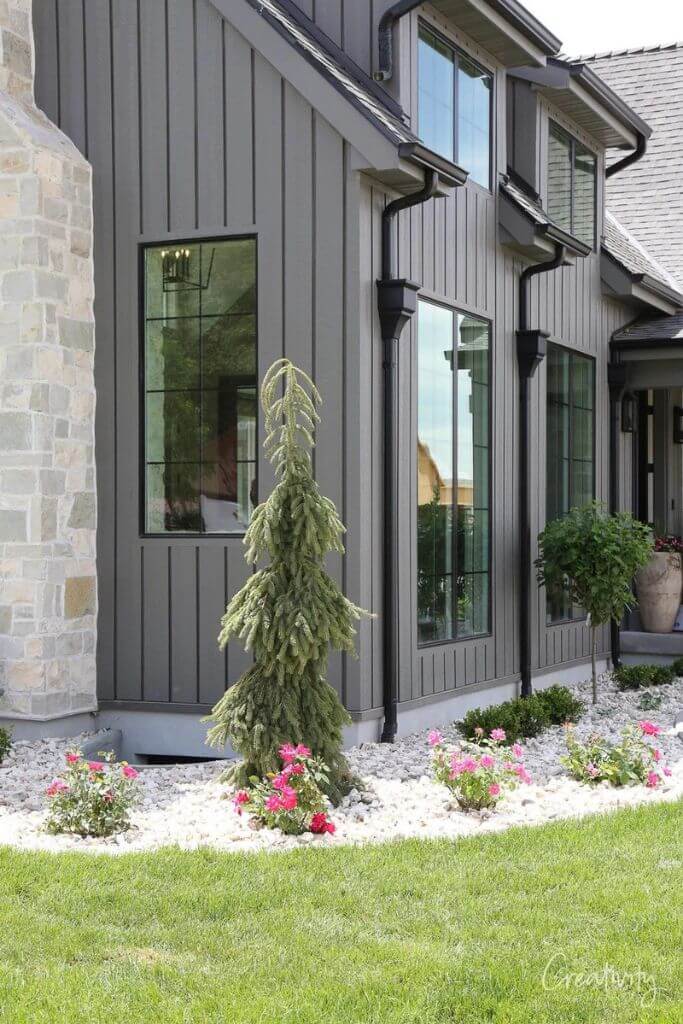 A home exterior with grey and stone siding with small plants in front.