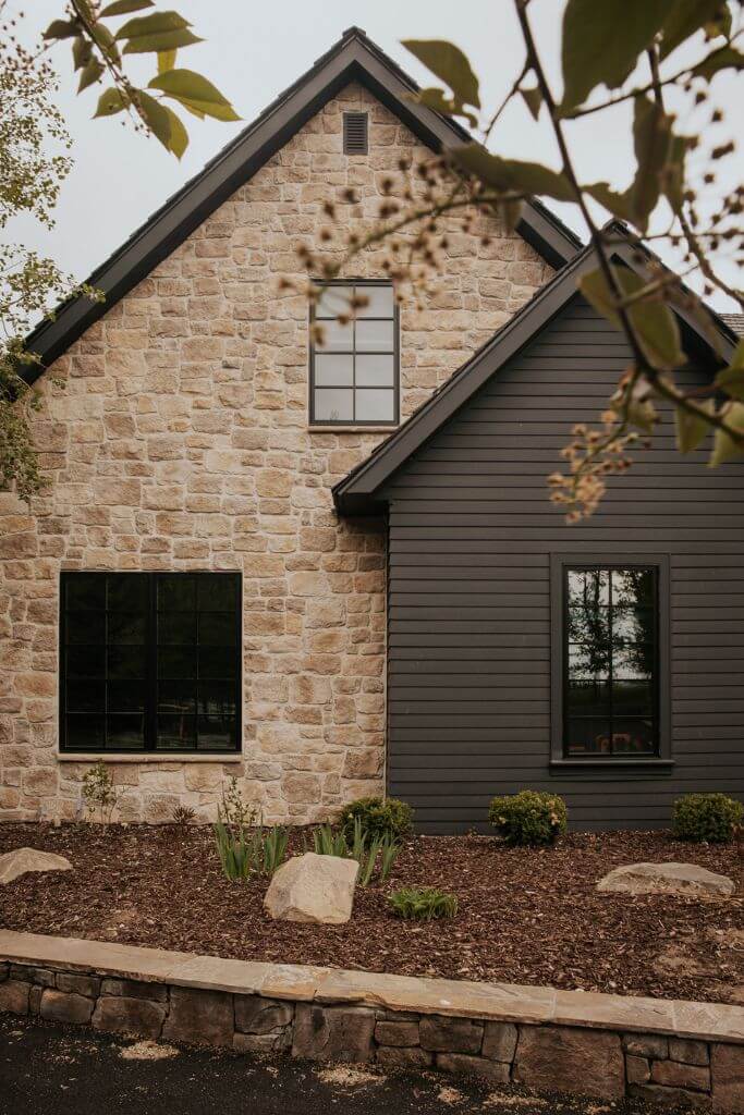 A home exterior with stone and dark grey siding with a rock planter out front.