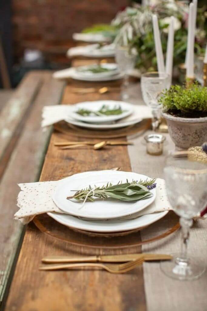 A wooden table set with white plates, lace napkins and greenery.
