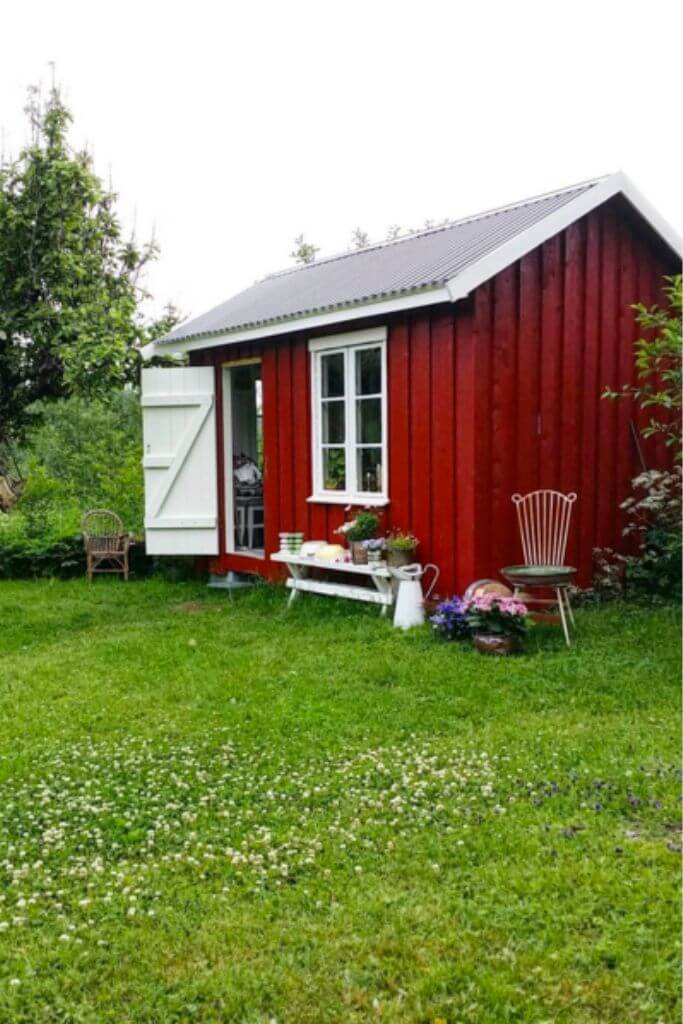 A red garden shed with a white door in a grassy field.