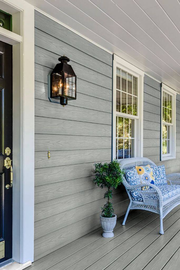 A home's front porch with grey siding and white wicker patio furniture.