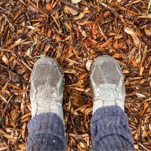 A pair of feet wearing green shoes standing on wood mulch.