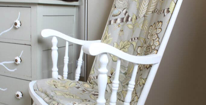 White rocking chair with patterned cushions in a neutral bedroom.