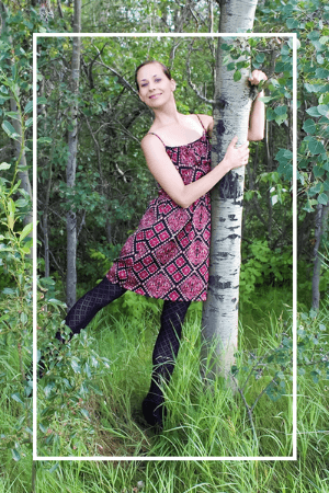 Larissa wearing a burgundy and navy patterned dress hugging a tree in a forest.